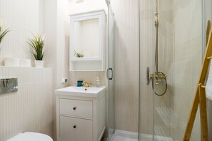 A modern bathroom with a glass-enclosed shower, a white vanity with a mirror, and a small plant on the counter. - ShortStayPoland Dąbrowszczaków B138 (Warsaw)