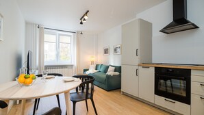 Moderni keittiö, jossa on sisäänrakennettu uuni, ruokailutila pöydän ja tuolien kera sekä taustalla oleva sohva.