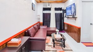 Ein modernes Hotelzimmer mit einer Couch, einem kleinen Tisch, einem Fernseher und einem Fenster mit Vorhängen.