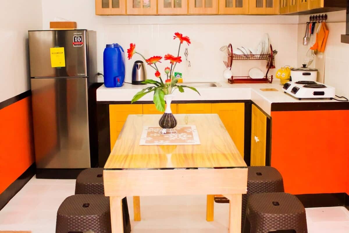 Eine Küche mit Holzausstattung, einem Edelstahlkühlschrank, einem Esstisch mit zwei Hocker und einer Vase mit Blumen.
