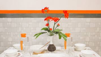Una mesa de comedor dispuesta con platos blancos, tazones y una jarrón transparente con etiqueta naranja.