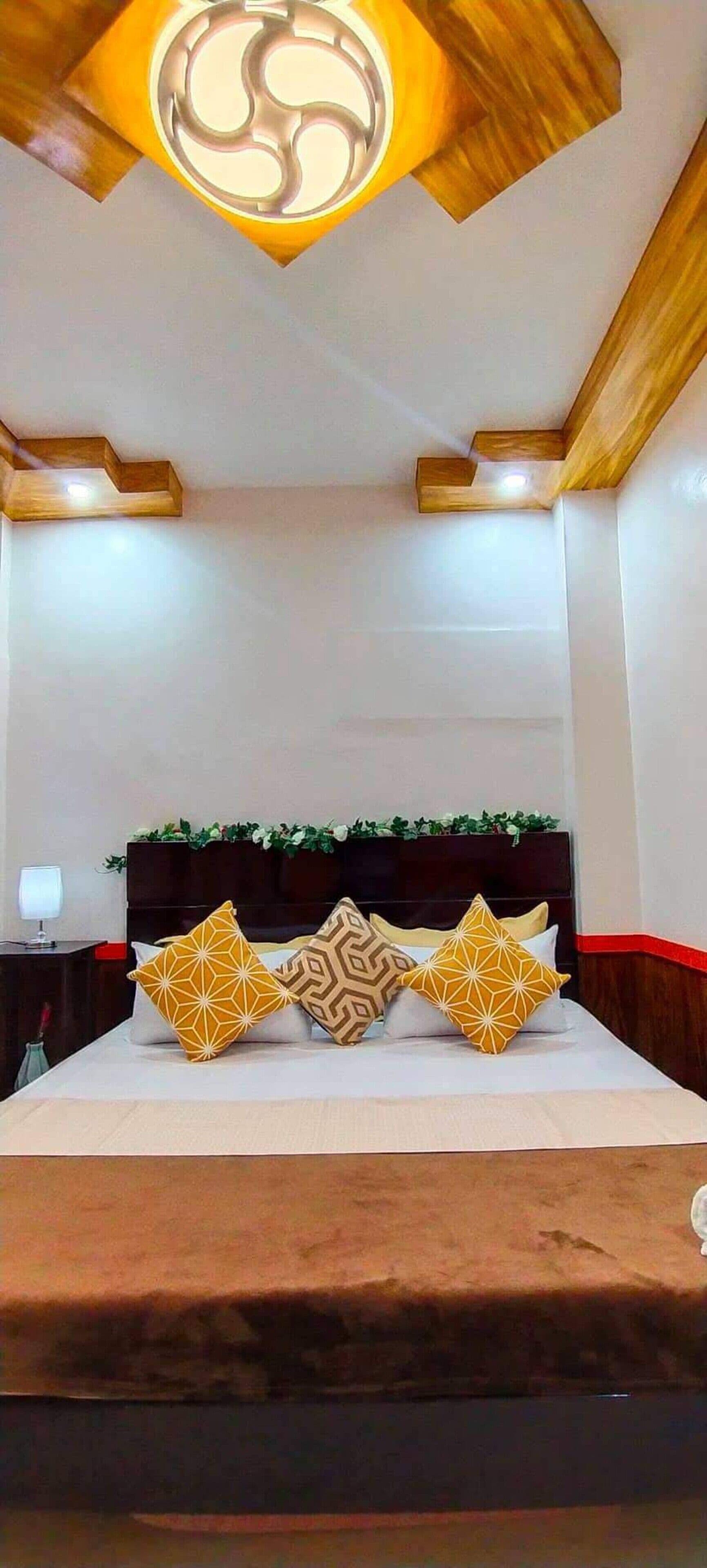 A bedroom with a bed, a headboard with a decorative top, and a ceiling light fixture.