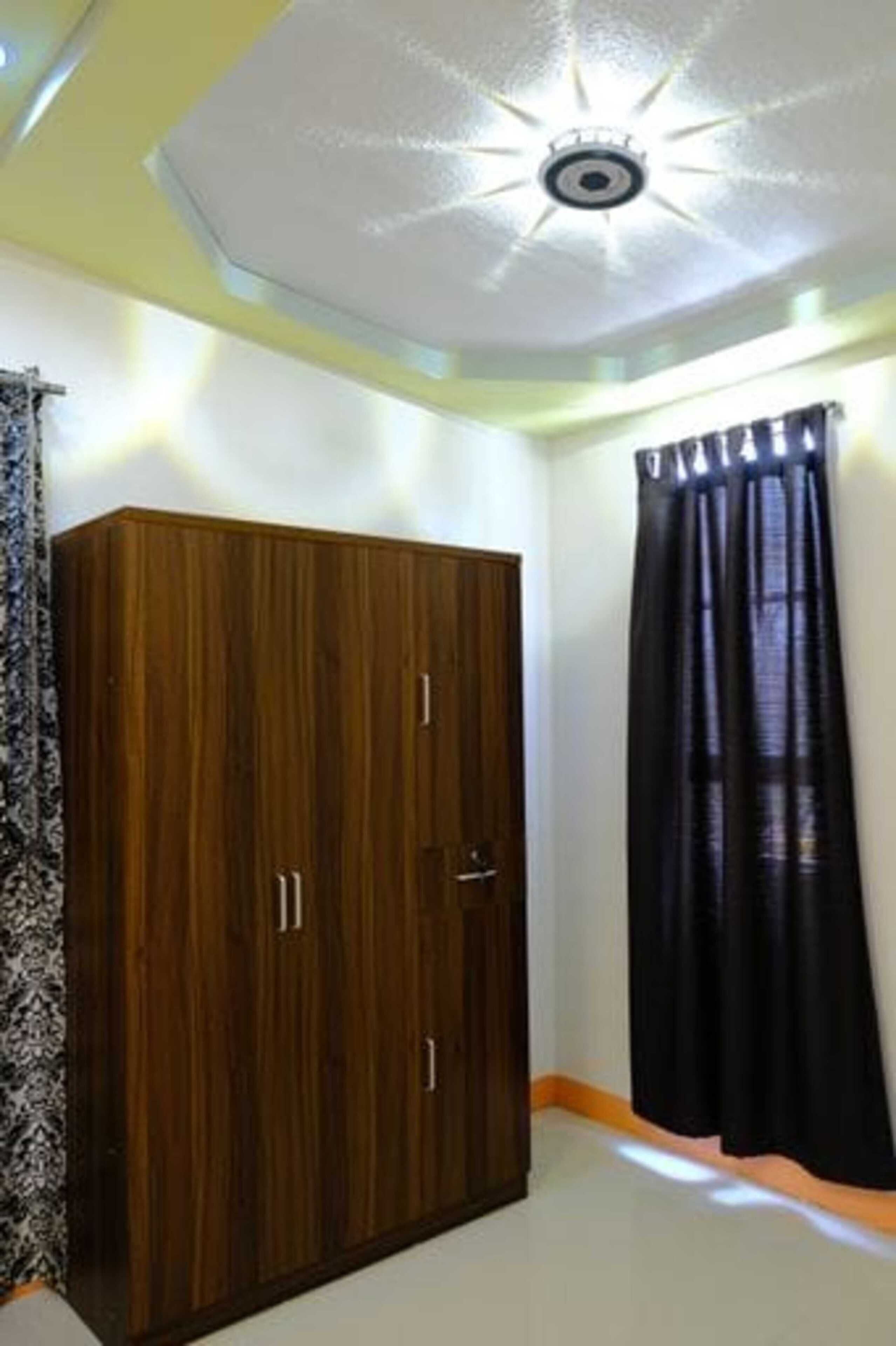 Una habitación con un armario de madera, una lámpara en el techo y una cortina negra.