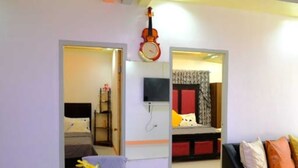 Ein Hotelzimmer mit einem Bett, einem an der Wand befestigten Fernseher, einer Uhr und einem kleinen Tisch mit einer Blumenvase.