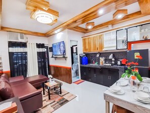A modern kitchen with wooden cabinets, a black countertop, and a dining area with a table set for four. - RB Modern Condos (Zamboanga)