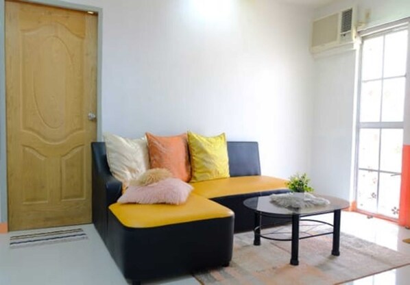 A living room with a sofa, a coffee table, and a door. - RB Modern Condos (Zamboanga)