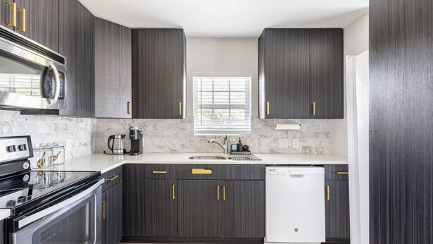 A modern kitchen with dark cabinetry, a stainless steel stove, a dishwasher, and a marble backsplash. - Welcome to Unit B (Houston)