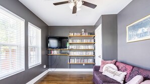 A living room with a bookshelf, a television, and a purple sofa with pillows. - Welcome to Unit B (Houston)