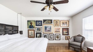 A bedroom with a large bed, a ceiling fan, and a wall of framed artwork. - Welcome to Unit B (Houston)