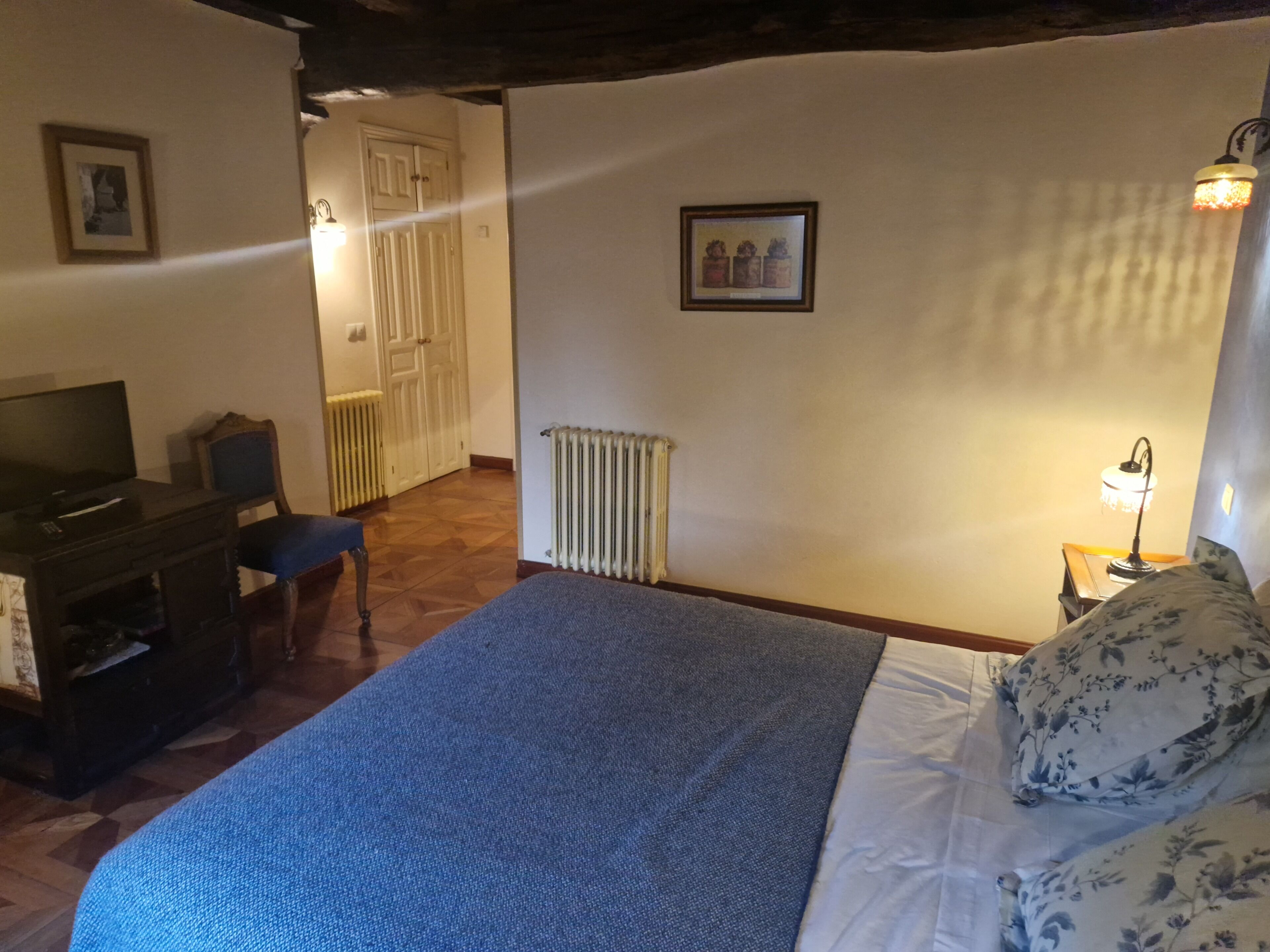 Een slaapkamer met een bed, een bureau, een stoel, een radiator en een wandlamp.