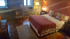 Un dormitorio acogedor con pared de piedra, una silla de madera, una cama con almohadones estampados y una mesita de noche con lámpara.
