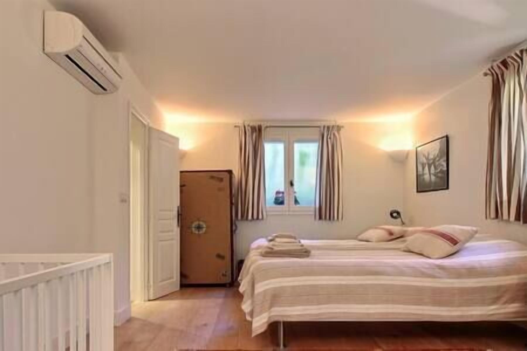 Un dormitorio con cama, ventana con cortinas, una puerta y un equipo de aire acondicionado.
