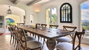 Un comedor amplio con una larga mesa de madera y múltiples sillas, ventanas grandes con diseños en arco y vistas al exterior.