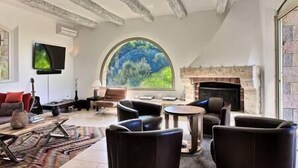 Amplia sala de estar con chimenea, asientos cómodos, un ventanal con vistas y vigas de madera a la vista en el techo.