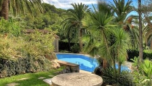 Un patio trasero con piscina, rodeado de exuberante vegetación y una mesa de piedra.
