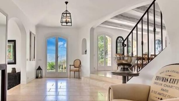 Un interior espacioso con techo alto, una escalera con barandilla de vidrio y un ventanal que ofrece vistas al verdor.