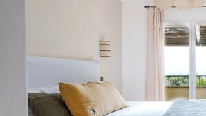 A bedroom with a bed, a wooden nightstand, a wall-mounted lamp, and a view of the outdoors through a sliding door. - Luxury villa in Gordes With Exceptional Views, Not Overlooked, Sleeps 16 (MURS)