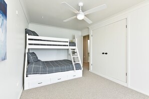 Ein Stockbett mit Stauraumschubladen, einem Deckenventilator und einem Kleiderschrank in einem Zimmer mit Teppichboden.