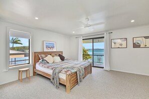A bedroom with a bed, a ceiling fan, a window with a view of the sea, and artwork on the walls. - Silverwater Serenity Shores Absolute Waterfront (Silverwater)