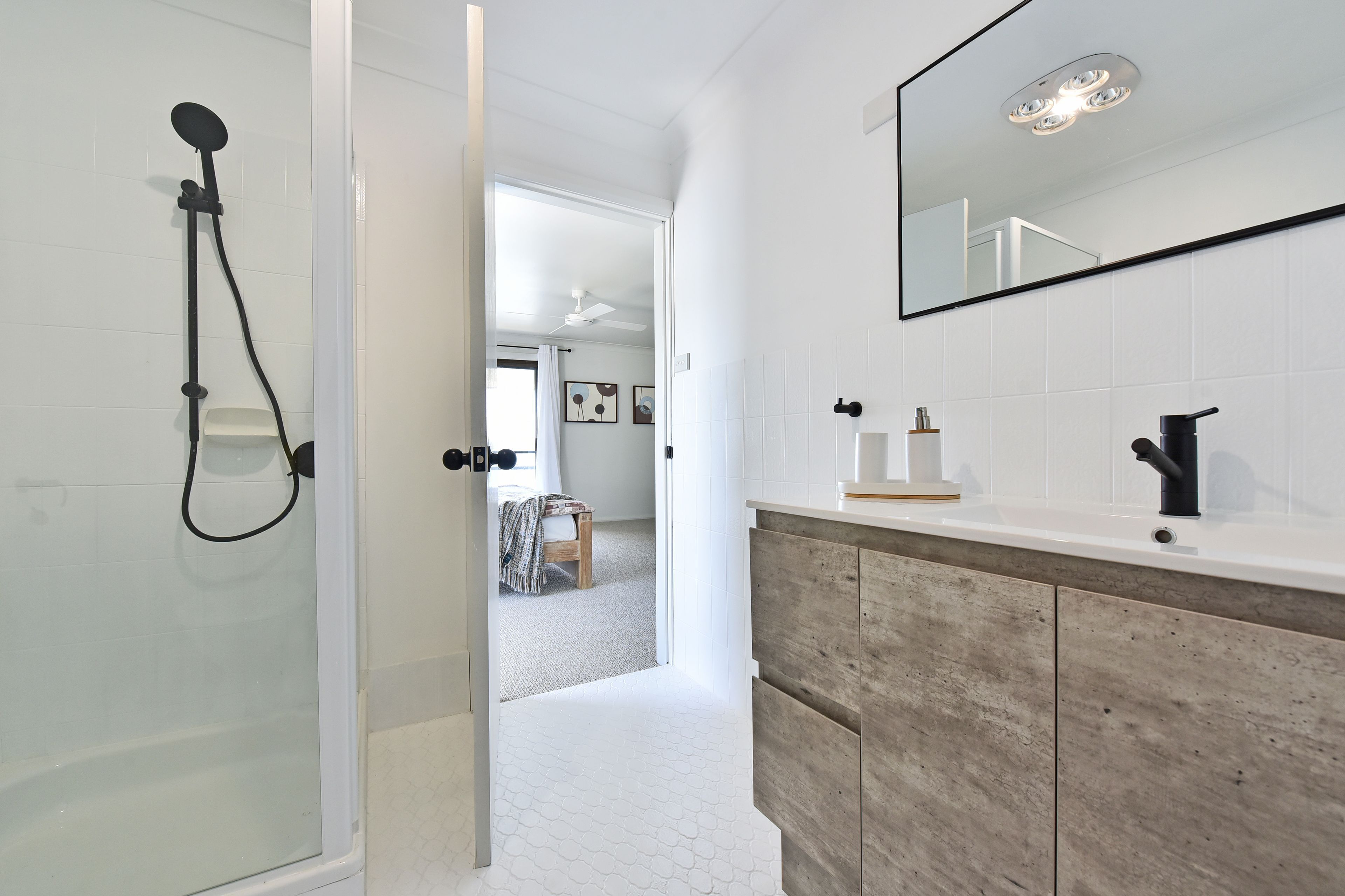 Een badkamer met een douche, een spiegel en een wastafelmeubel met een houten kastje.