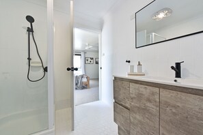 A bathroom with a shower, a mirror, and a vanity with a wooden cabinet. - Silverwater Serenity Shores Absolute Waterfront (Silverwater)