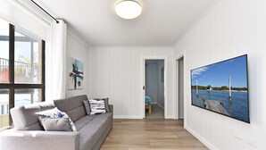 A modern living room with a grey sofa, a painting, and a large TV screen displaying a scenic view. - Silverwater Serenity Shores Absolute Waterfront (Silverwater)