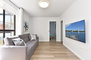 Ein modernes Wohnzimmer mit einem grauen Sofa, einem Gemälde und einem großen Fernseher, der eine schöne Landschaft zeigt.
