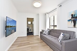 A modern living room with a grey sofa, a flat-screen TV, and a painting on the wall. - Silverwater Serenity Shores Absolute Waterfront (Silverwater)