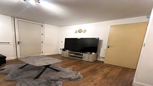 A living room with a flat-screen TV, a grey sofa, a coffee table, and a shaggy rug.