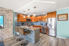 A kitchen with a central island, wooden cabinets, stainless steel appliances, and pendant lighting. - Modern King Suite, Pool & Hot Tub, Steps to Beach (Kihei)