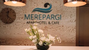 Un espace d’accueil avec un mur en bois, une horloge et une enseigne indiquant « Merepargi Apartment Hotel & Cafe ».