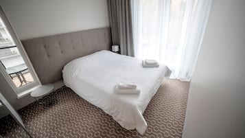 A hotel room with a large bed, a bedside table, a window with curtains, and a patterned carpet.