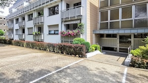 Um edifício com vários andares, varandas, área de estacionamento e entrada com portão.