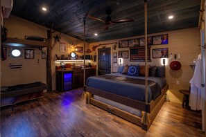 A room with a bed, a desk with a computer, a ceiling fan, and wooden walls. - Two Treehouses + Bridge | Double 20-Foot Slides | Smoky Mountain Views (Sevierville)