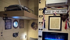 A bunk bed room with a small bed, a wall-mounted air conditioner, a framed document, and patriotic decorations. - Two Treehouses + Bridge | Double 20-Foot Slides | Smoky Mountain Views (Sevierville)