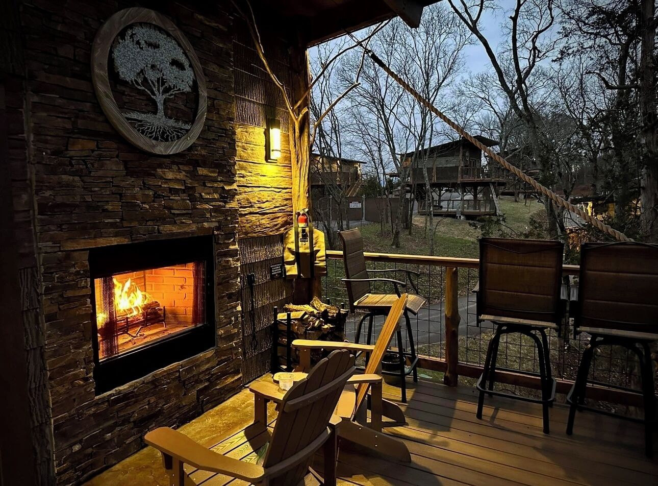 A cozy outdoor seating area with a stone fireplace, wooden deck, and chairs.