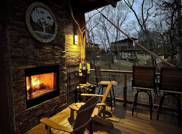 A cozy outdoor seating area with a stone fireplace, wooden deck, and chairs.