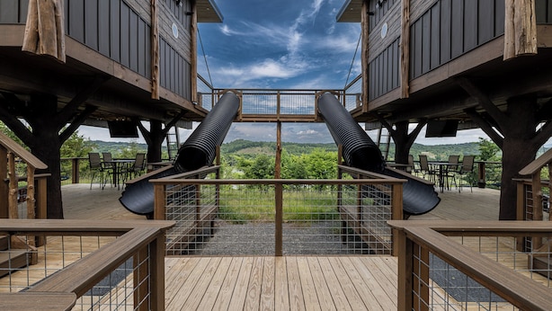 A wooden deck with a central viewing platform, surrounded by tables and chairs, overlooking a scenic landscape. - Two Treehouses + Bridge | Double 20-Foot Slides | Smoky Mountain Views (Sevierville)