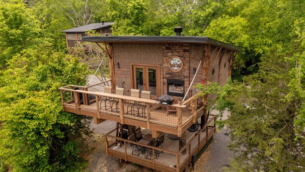 A wooden cabin with a deck, outdoor seating, and a fireplace. - Luxury Treehouse | Golf + Smoky Mountain Views | Slide | Sleeps 6 (Sevierville)