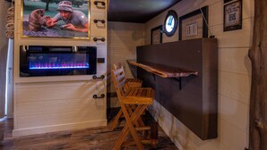 A room with a wooden floor, a mounted television, a fireplace, and a wooden chair. - Luxury Treehouse | Golf + Smoky Mountain Views | Slide | Sleeps 6 (Sevierville)