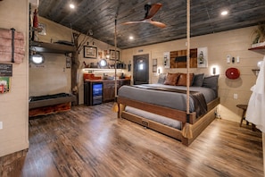 A rustic room with a bed, wooden floors, a ceiling fan, and a small kitchenette. - Luxury Smoky Mountain Treehouse | 20-Foot Slide | Sleeps 6 | Near Dollywood (Sevierville)