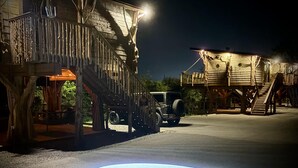 A treehouse resort with wooden structures, a Jeep, and a circular logo on the ground. - Smoky Mountain Luxury Treehouse | 20-Foot Slide | Secret Beds | Sleeps 6 (Sevierville)