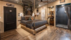 A room with a bed, a wooden door, a mirror, and a shower area. - Smoky Mountain Luxury Treehouse | 20-Foot Slide | Secret Beds | Sleeps 6 (Sevierville)