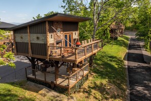 A wooden cabin with a deck, outdoor seating, and a grill area.