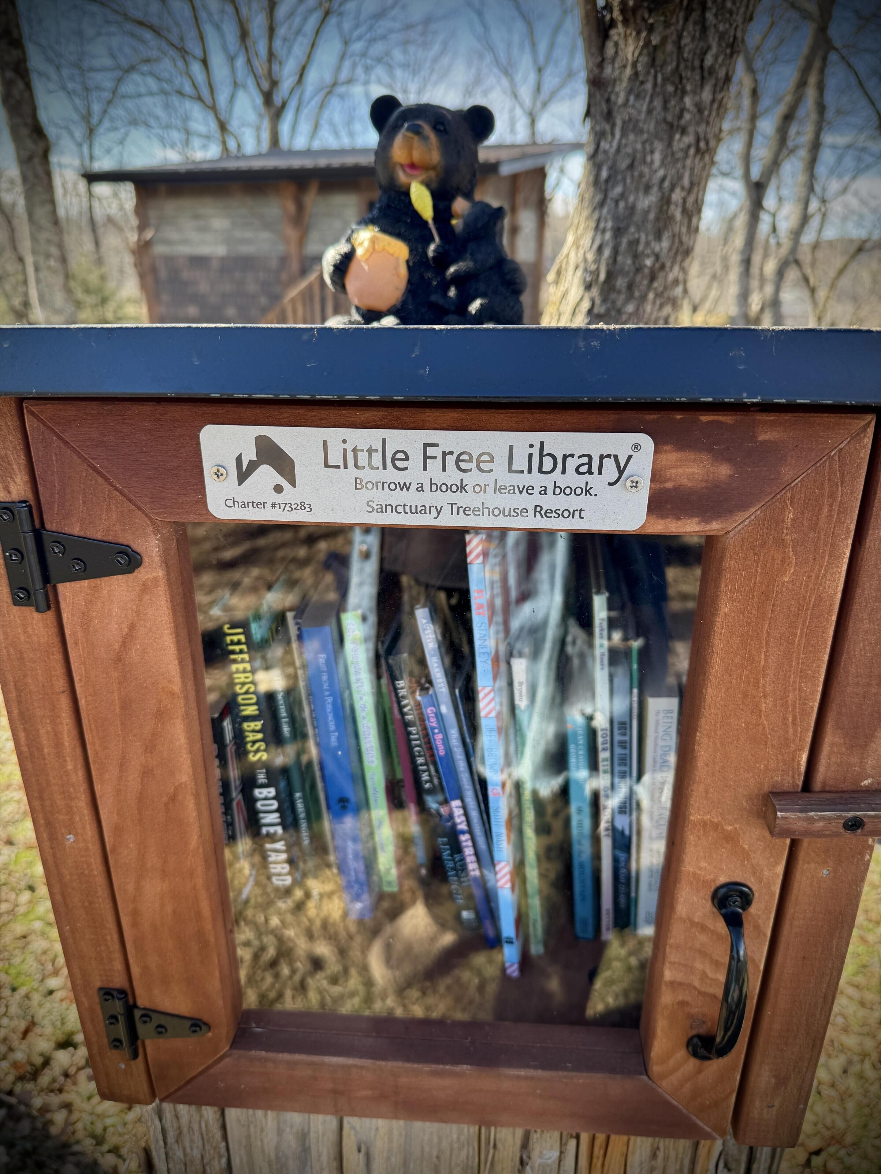 Une structure en bois surmontée d’une figurine d’ours et portant une pancarte indiquant « Petite bibliothèque gratuite ».