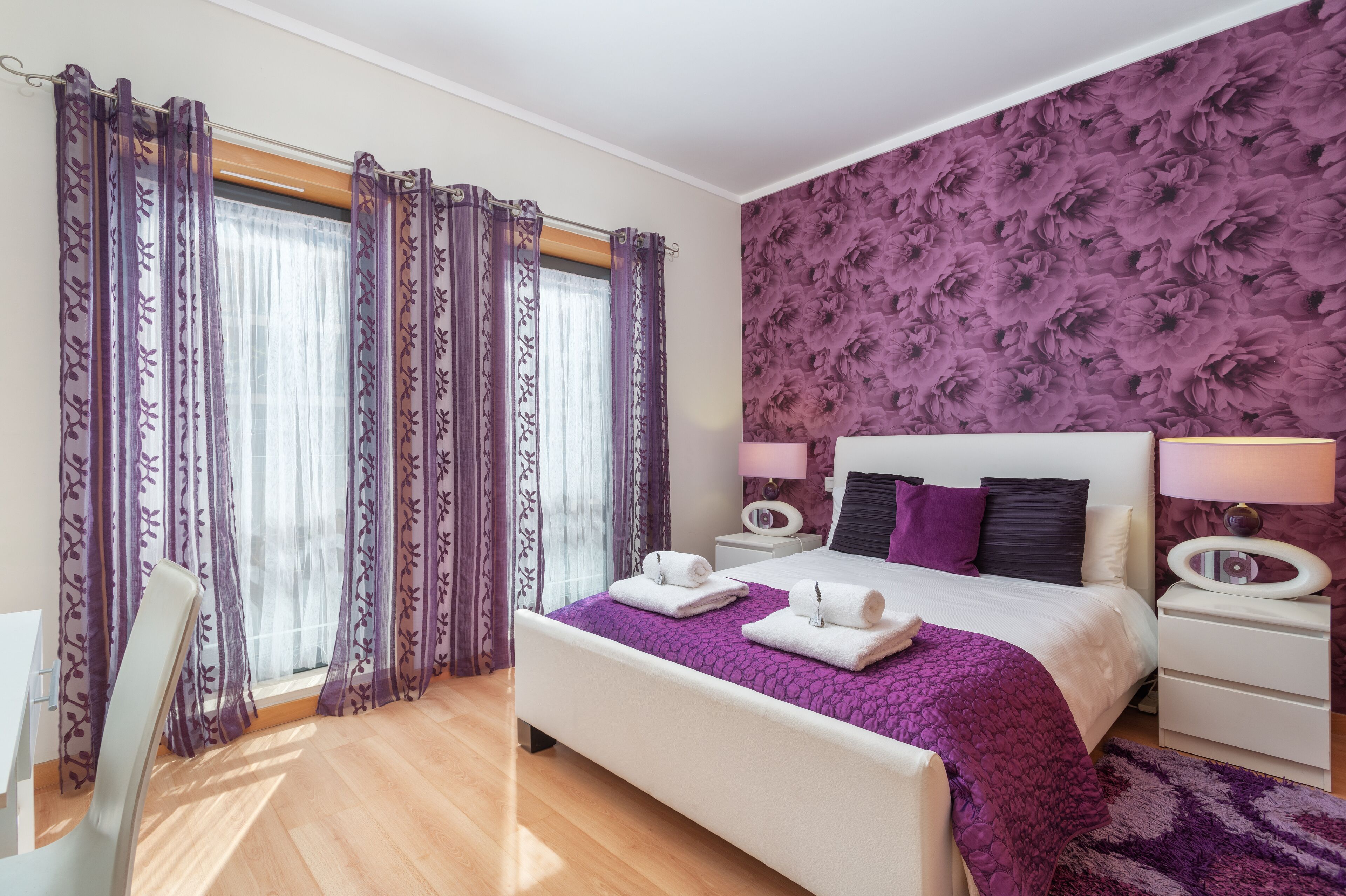 A bedroom with a bed, nightstands, a chair, and a window with curtains.