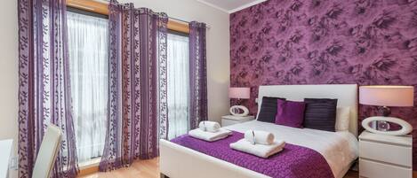 A bedroom with a bed, nightstands, a chair, and a window with curtains.