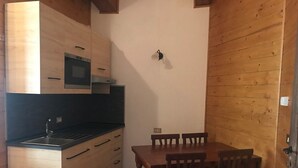 Cocina compacta con armarios de madera, encimera negra y horno pequeño. Cuenta con una mesa de comedor con cuatro sillas y una lámpara fijada a la pared.