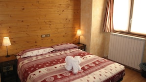 Una habitación acogedora con paredes de madera, una cama con ropa de cama estampada, dos lámparas de noche y una ventana con cortinas.