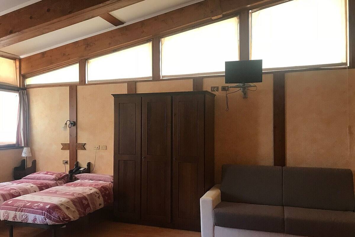 A room with a wooden ceiling, a large wardrobe, a sofa, and a bed with patterned bedding.